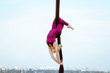 exercises with aerial silk outdoor, sky background. beautiful fit woman training acrobatic in airt. 