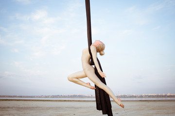 exercises with aerial silk outdoor, sky background. beautiful fit woman training acrobatic in airt. 