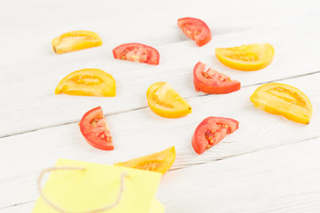 Poured out of paper bag slices of red and yellow ripe fresh tomatoes on old white rustic wooden planks