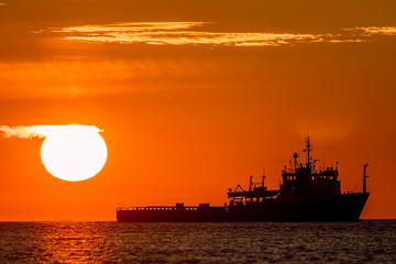 Tropical sunrise or sunset at sea. Calm ocean image of a ship on the horizon.