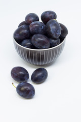 Plums in a bowl, separated, close up. White background.