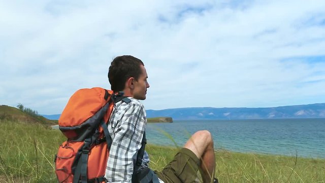 Hiker relaxing on a shore of lake Baikal. Traveler young brunette man looking at blue water. Olkhon Island, Baikal, Russia, Siberia