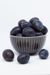 Plums in a bowl, separated, close up. White background.