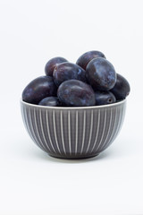Plums in a bowl, separated, close up. White background.