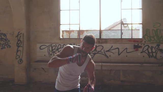 Muscular male boxer doing shadow boxing exercise in an old abandoned building