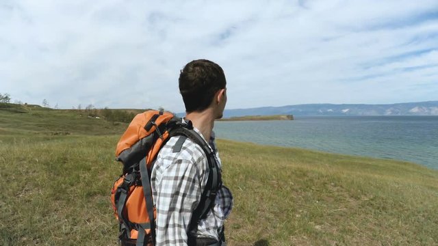 Hiker standing on a shore of Baikal. Traveler young brunette man looking at lake. Olkhon Island, Baikal, Russia, Siberia