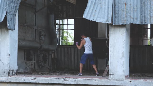 Muscular male boxer doing boxing exercise among abandoned factory rubble. Slow motion.