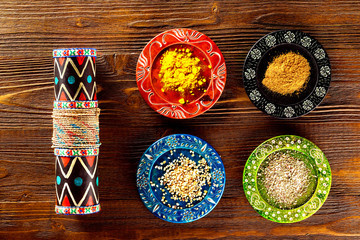 Closeup image of colorful ethnic style plates with spices and maraca at wooden table background.