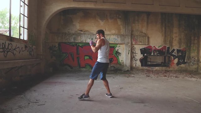 Male boxer doing shadow boxing exercise in an old abandoned building. Slow motion.