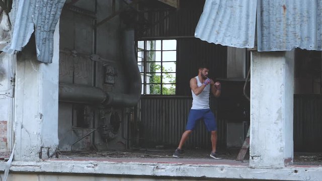 Muscular male boxer doing boxing exercise in an old abandoned factory. Slow motion.