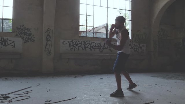 Muscular male boxer doing shadow boxing exercise in an old abandoned building. Slow motion.
