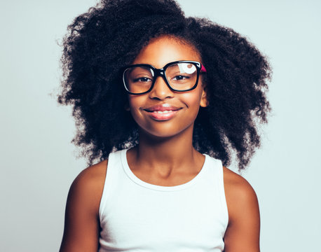 Smiling young African girl wearing glasses against a gray backgr