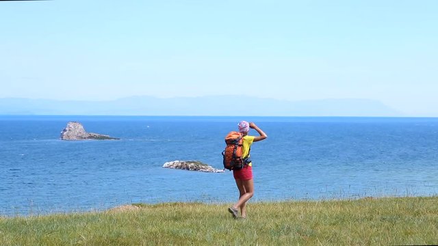 Hiking woman with backpack trekking along blue lake Baikal. Caucasian girl living active lifestyle