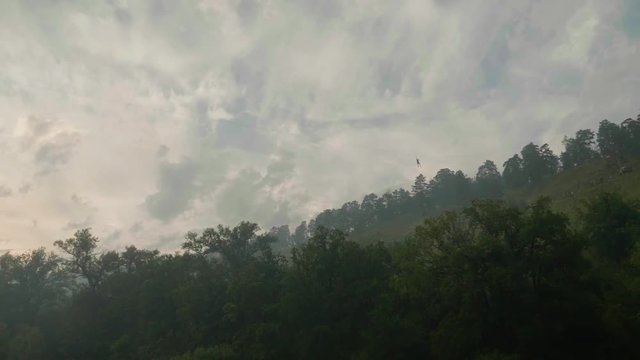 Man riding zip line in mountains at height of several metres from right to left with grey sky behind
