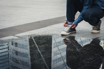 handsome man sit on concrete floor tying shoelace to wearing the shoes with  water reflection on floor.