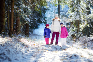 Two adorable little girls and their mother having fun together in beautiful winter park. Beautiful sisters playing in a snow.