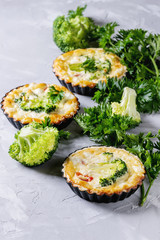 Baked homemade vegetable broccoli quiche pie in mini metal forms served with fresh greens on gray concrete background. Close up. Ready for eat