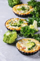 Baked homemade vegetable broccoli quiche pie in mini metal forms served with fresh greens on gray concrete background. Close up. Ready for eat