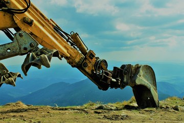 riesiger bagger arm vor bergpanorama/eingriff des menschen in die natur/ berge und maschienen, zerstörung der natur und natürlicher lebensräume