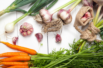 Fresh vegetables, garlic, onions and carrots on a white wooden table. View from above.