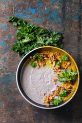 Mushroom cream soup in black ceramic bowl served with turmeric powder, forest mushrooms, greens parsley, fried onion over old dark wooden background. Top view