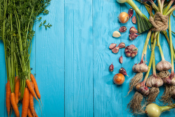 Fresh carrots, garlic and onions on a blue background