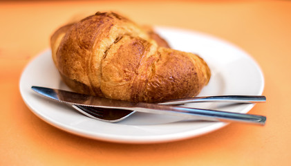 freshly made croissant on the plate with knife and fork on the orange background
