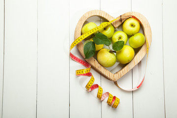 The concept of diet and healthy eating. A green apple and a centimeter on a white wooden background in the heart. - 170866093