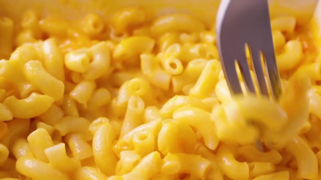 Close video of macaroni and cheese in a microwavable paper tray being slowly stirred with a fork after heating..