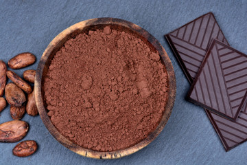 Cacao powder in a bowl with beans and chocolate on slate