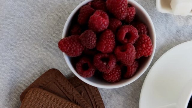 Healthy breakfast - cup of black coffee, bowl of raspberries, bowl of yogurt or milk with fruits, berries and granola or gorp. Top view.	Slow pan.