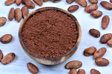Cacao powder in a bowl with beans on wooden table
