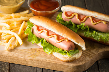 Tasty barbecue grilled hot dog with salad,yellow mustard, onion, ketchup, and French fries on wooden background. Junk and fast food concept.