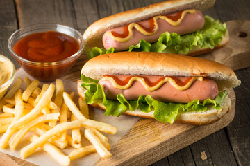 Tasty barbecue grilled hot dog with salad,yellow mustard, onion, ketchup, and French fries on wooden background. Junk and fast food concept.