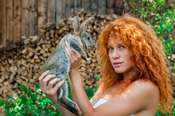 Beautiful girl with red hair on nature with a rabbit in her hands