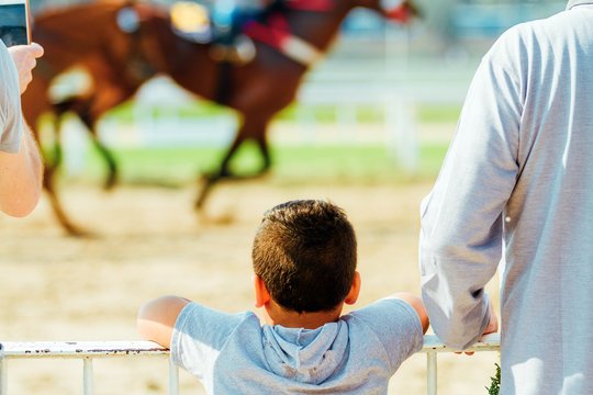Child looking at a horse race next to an adult and horse on background