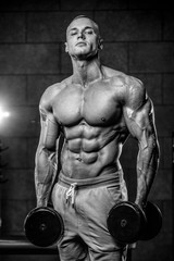 Fototapeta na wymiar Brutal Caucasian bodybuilder training shoulders in gym..