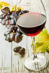 Бокал красного вина, красный виноград, листья винограда на старом деревянном столе 