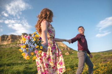 Young married couple. The guy leads a curly girl with a bouquet of flowers.