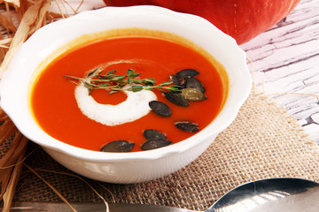 Roasted pumpkin and carrot soup with cream and pumpkin seeds on wooden background.
