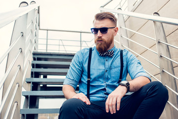 young guy with a beard and mustache with glasses posing on the street in the sunlight, fashion man, style, vintage style, retro men, handsome beard, outdoor portrait, hipster man