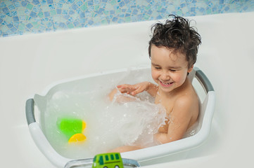 a happy child bathes in a bathroom. Little baby having soapy bath at home