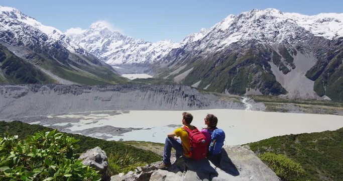 Hikers looking at view. Active hiking couple outdoors in mountains relaxing enjoying resting during hike. Young couple on trail by Mt Cook in Aoraki / Mount Cook National Park. RED EPIC.