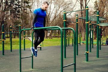 Young strong man doing the exercises on the uneven bars on the sports field in the summer in the city