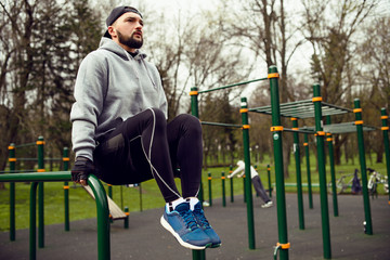 Young strong man doing abs exercises  on the uneven bars on the sports field in the summer in the city