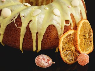 Danish carrot cake with icing and candied fruit closeup on black background