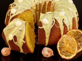 Sliced Danish carrot cake with icing and candied fruit on black backround