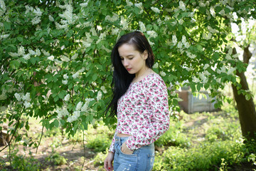 adorable beautiful young brunette woman posing in the garden with flowering trees on a beautiful sunny day