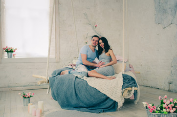 Naklejka premium happy family of pregnant woman and young husband sitting on bed