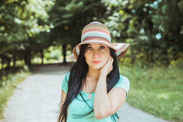 adorable beautiful young brunette woman posing in the garden in a big hat on a beautiful sunny day
